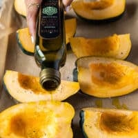 A hand pouring olive oil over the squash to season it before roasting