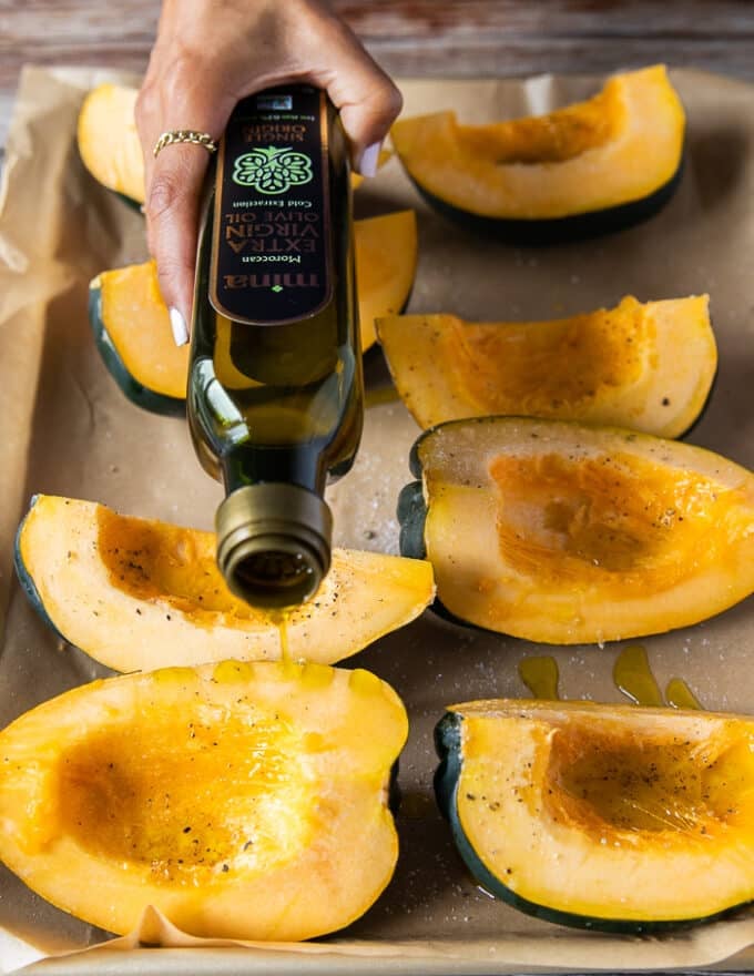 A hand pouring olive oil over the squash to season it before roasting