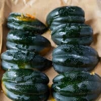 Acorn squash arranged on a baking sheet cut side down and ready to go in the oven