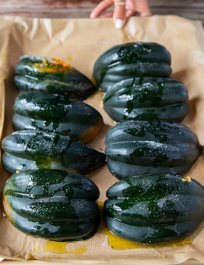 Acorn squash arranged on a baking sheet cut side down and ready to go in the oven