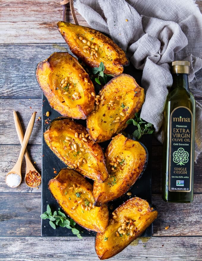 The roasted acorn squash on a board right out of the oven and some pine nuts is sprinkled on top