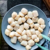 Seasoned scallops in a bowl with salt, pepper and olive oil