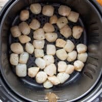 Scallops arranged in a single layer in the air fryer basket ready to cook