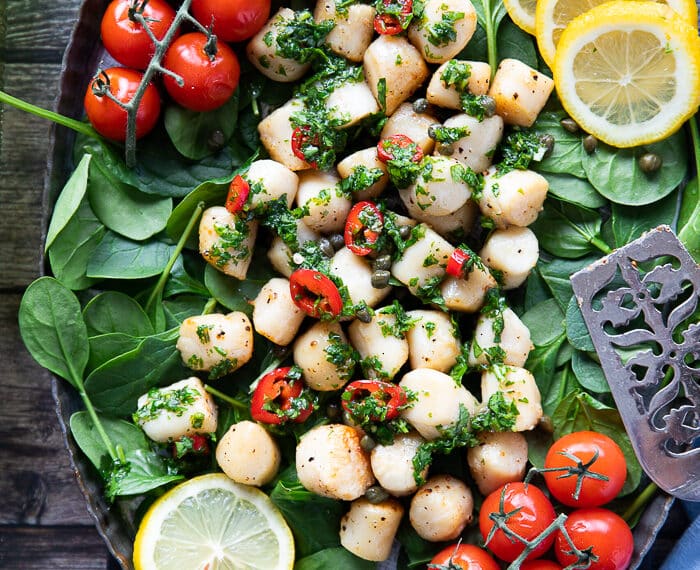 A plate of air fryer scallops over a bed of spinach, tomatoes, and drizzled with chimichurri sauce