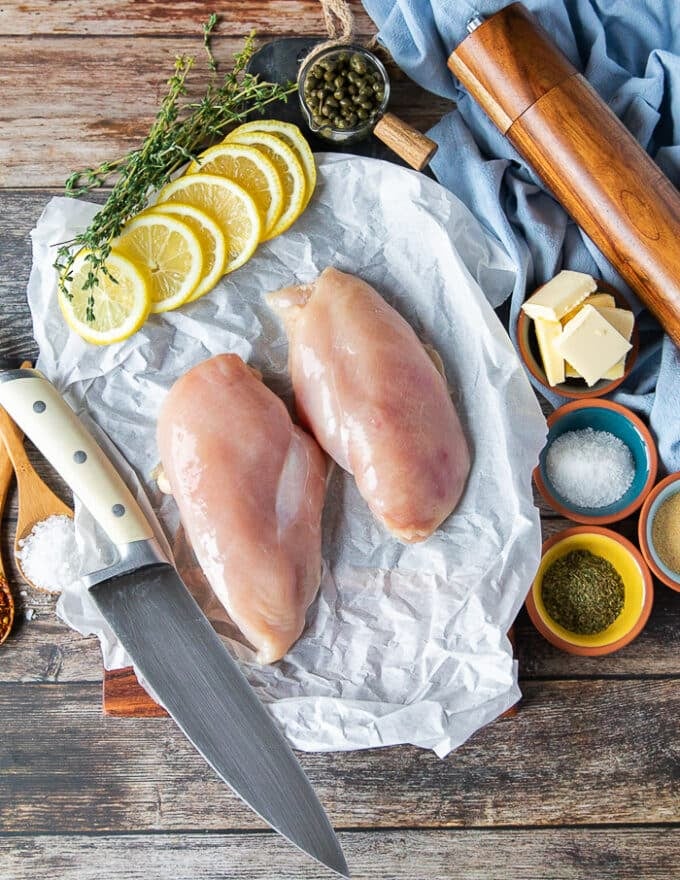 Ingredients for chicken scallopini recipe including chicken breast, a knife, lemon, capers, butter, lemon juice, stock, seasoning and flour bowl