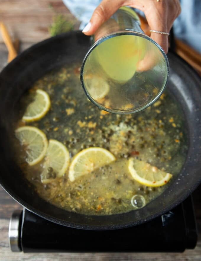 A hand pouring in some stock to finish off the chicken scallopini sauce