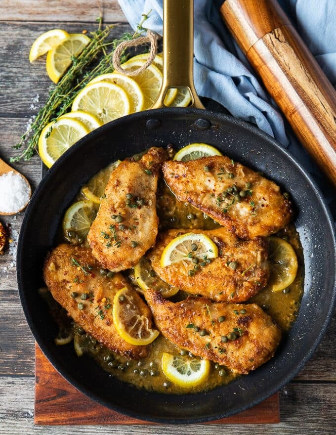 A skillet with chicken scallopini cooked up in it with lemon slices, capers and golden brown seared chicken breast 