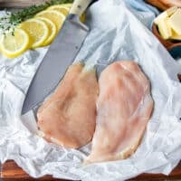 paper thin chicken breasts sliced on a parchment paper ready for breading to make chicken scallopini recipe