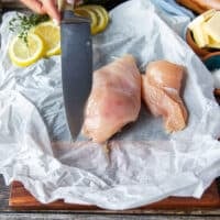 A knife slicing each chicken breast in half to make two thin chicken breasts
