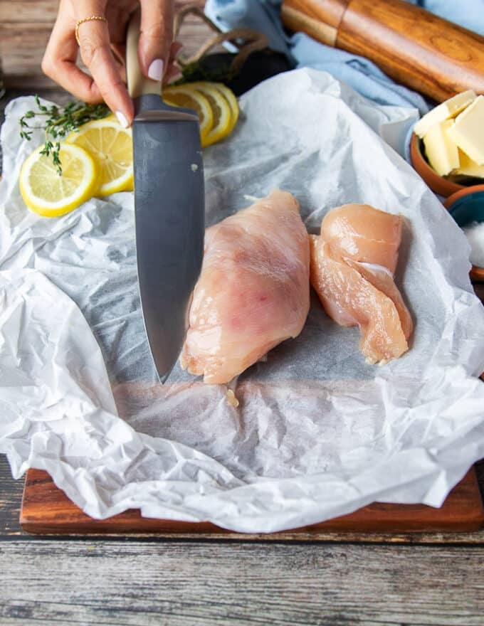 A knife slicing each chicken breast in half to make two thin chicken breasts 