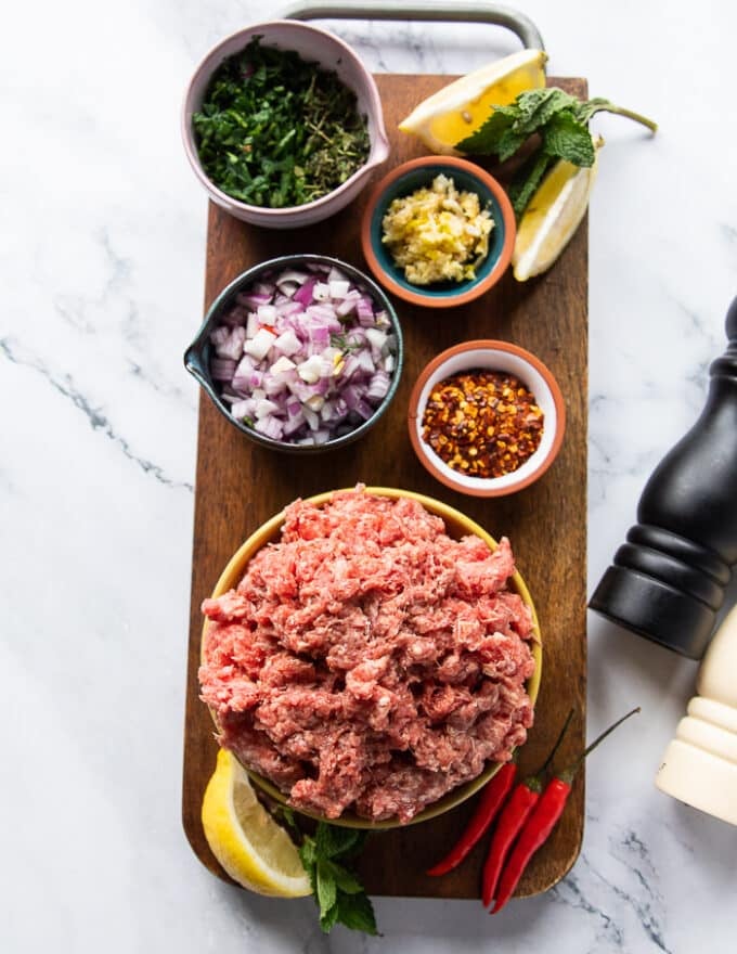 ingredients for making pita bowls with lamb including: ground lamb, onions, chilli flakes, salt and pepper, garlic, fresh herbs