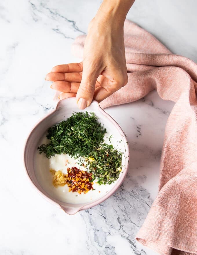 Yogurt sauce and tahini sauces ready and a hand holding a bowl of yogurt sauce