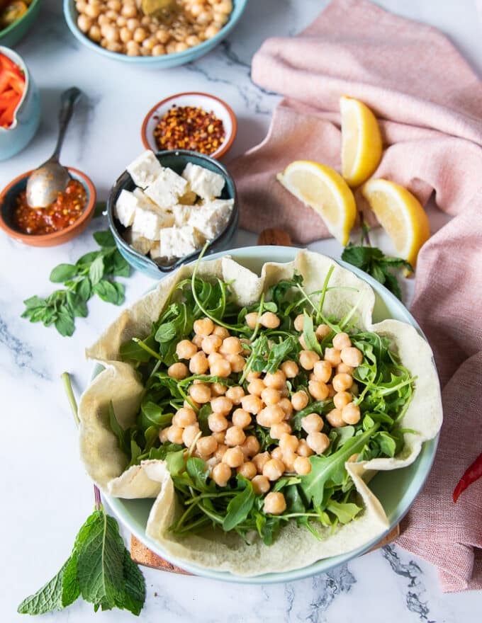 Arugula and chickpeas added over the pita bread to start building the pita bowl