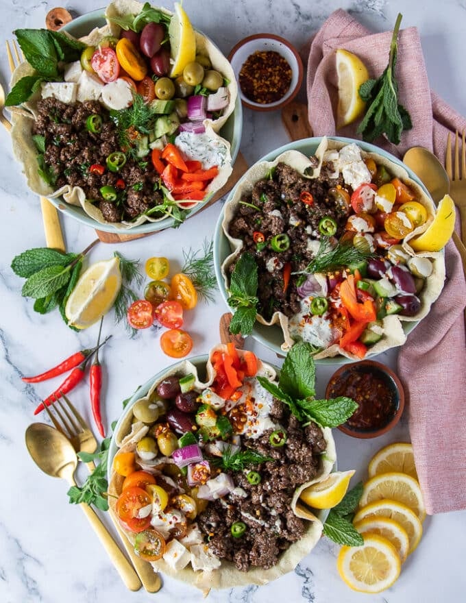 three pita bowls loaded and assembled on a white marble with many colorful toppings