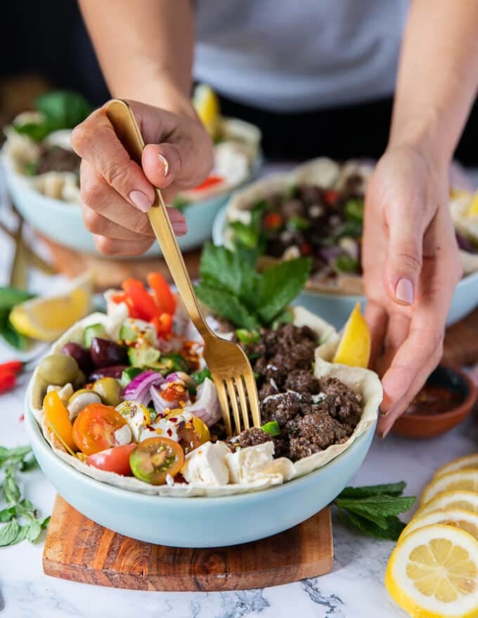 a hand taking the fork to dip it in the pita bowls and start eating