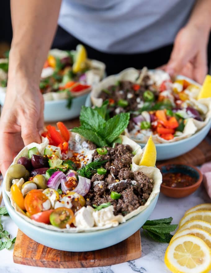 A hand holding two pita bowls loaded with toppings and lined iwth pita bread