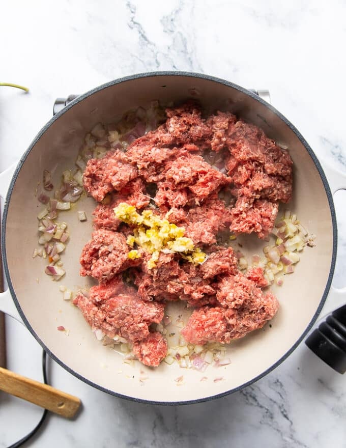 Ground lamb, garlic and seasoning are added to the cooked onions in a pan to make pita bowl topping