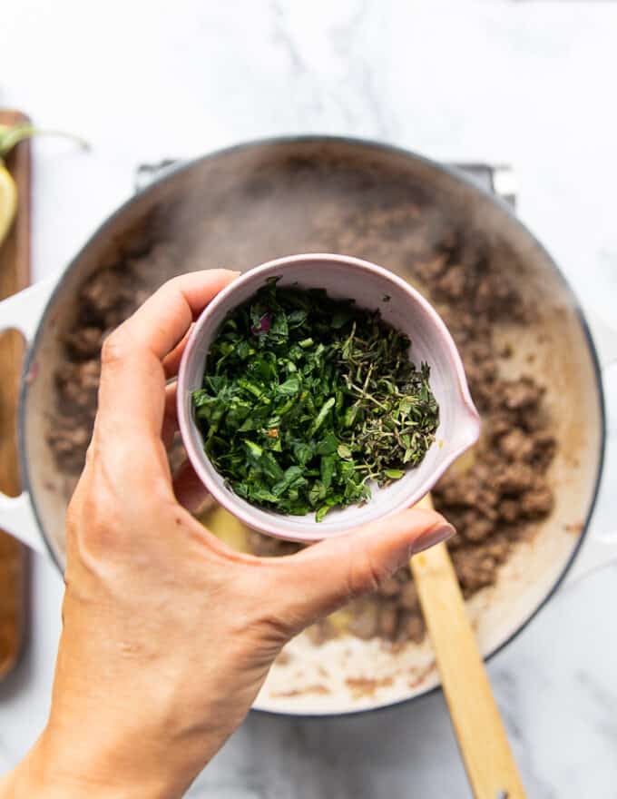 A hand holding a bowl of fresh herbs ready to add over the cooked lamb 