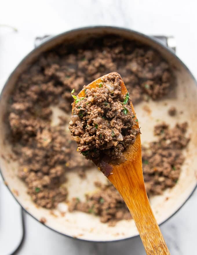 A wooden spoon showing a close up of the cooked ground lamb showing it's ready for the pita bowl