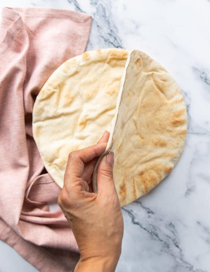 A hand holding a thin style pita bread showing the desired type of pita ideal to make pita bowls
