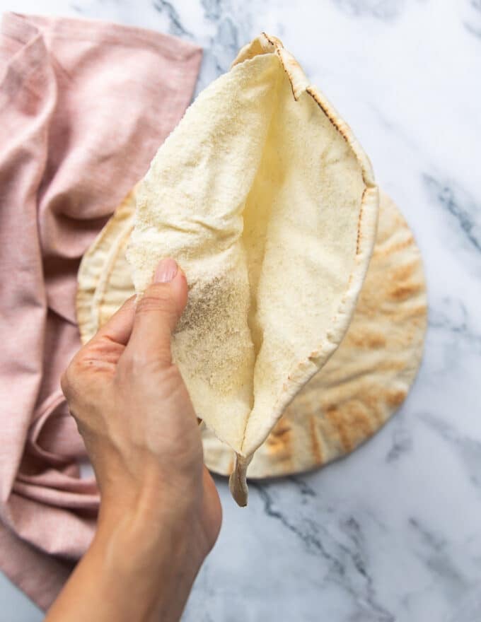 A hand splitting each pita bread into two by separating the layers