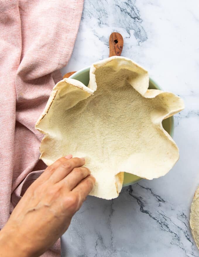 One half pita bread is added at the bottom of the pita bowl and pressed well