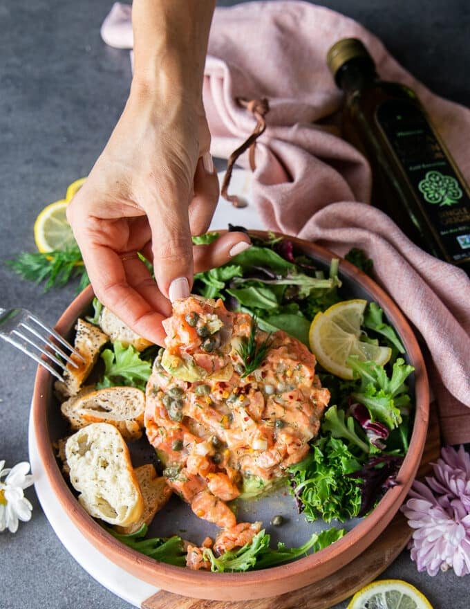 A hand showing a scoop of salmon tartare on a piece of bread 