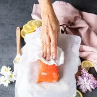 A hand patting down the salmon to make the tartare recipe with a paper towel