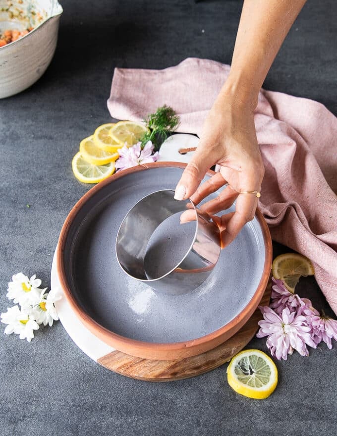 A hand holding a large round ring mold to stack up the salmon tartare