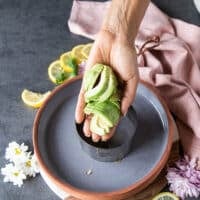 A hand holding the sliced avocados and ready to place them at the bottom of the mold to stack the salmon tartare recipe