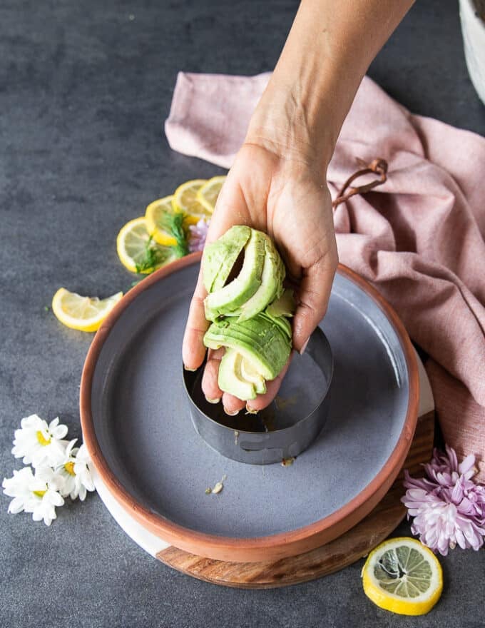 A hand holding the sliced avocados and ready to place them at the bottom of the mold to stack the salmon tartare recipe 