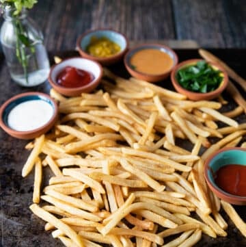 Air fryer frozen french fries on a sheet, showing crispy fresh french fries surrounded by many dipping sauces like hot sauce, ranch, chipotle, ketchup and more