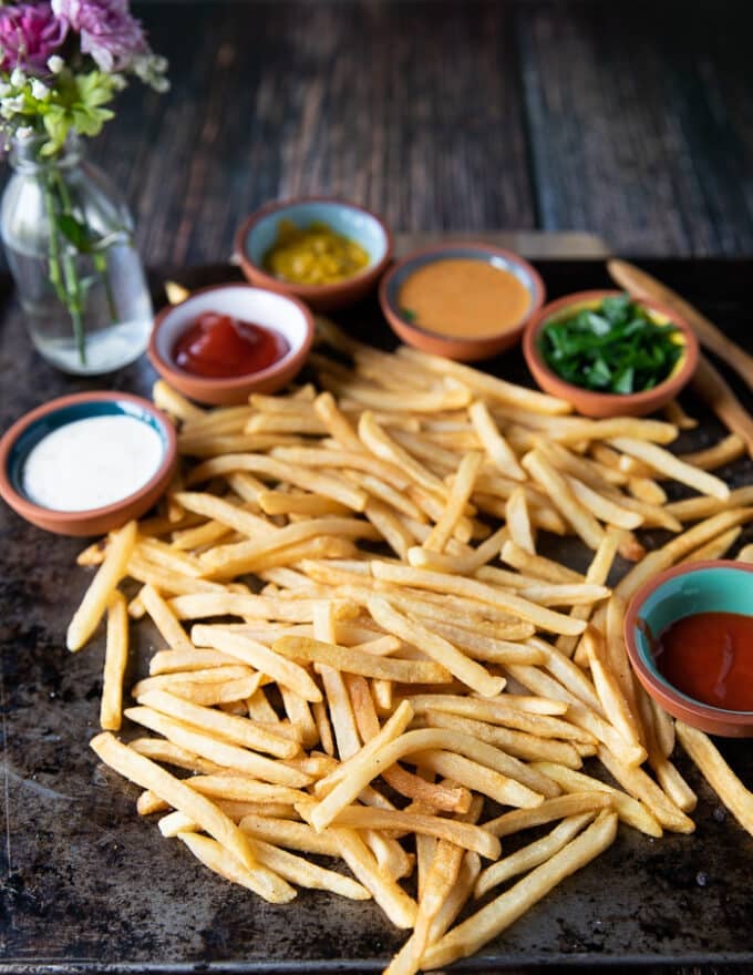 Air fryer frozen french fries on a sheet, showing crispy fresh french fries surrounded by many dipping sauces like hot sauce, ranch, chipotle, ketchup and more
