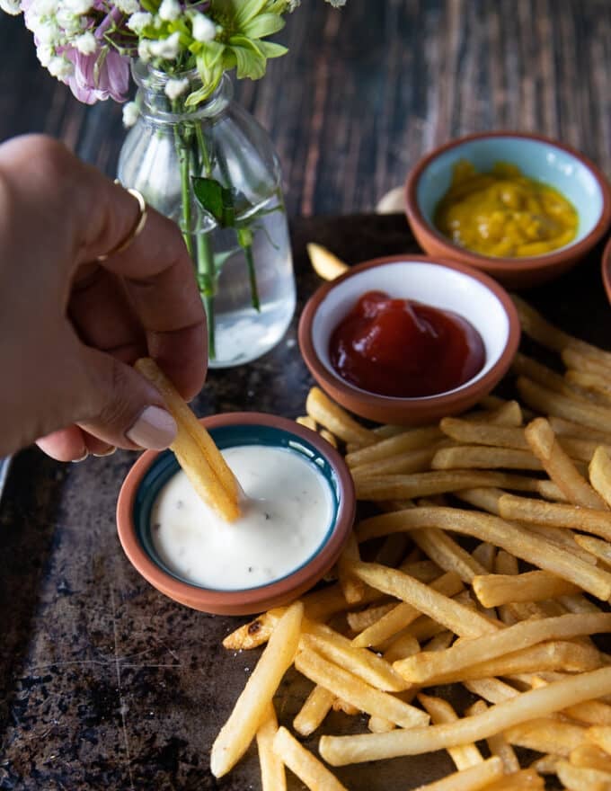 a hand dipping the french fries in a ranch dip bowl