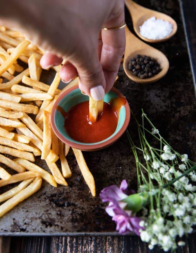 A hand dipping air fryer fries in hot Sriracha sauce!
