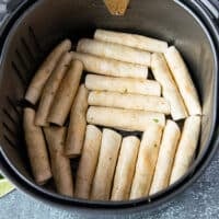 The rolled up taquitos in a single layer at the bottom of an air fryer basket.