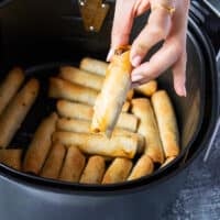 A hand holding one taquitos close up from the air fryer basket showing how crisp and golden the taquitos are in the air fryer