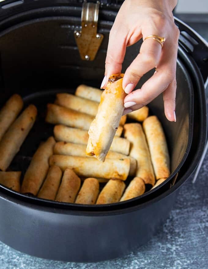 A hand holding one taquitos close up from the air fryer basket showing how crisp and golden the taquitos are in the air fryer