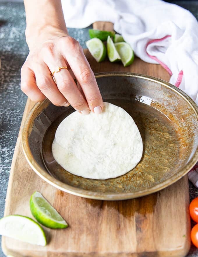 A hand dipping in the flour tortillas one by one into the plate with oil. 