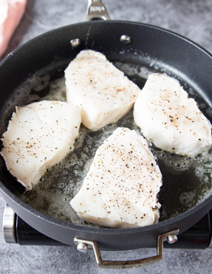 Chilean sea bass seasoned with salt and pepper in a hot skillet