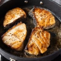 Flipped golden chilean sea bass fillets in a hot pan continuing to cook