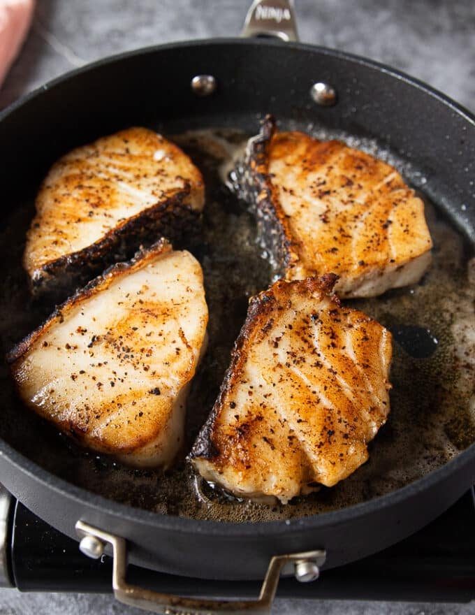 Flipped golden chilean sea bass fillets in a hot pan continuing to cook