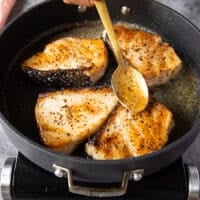 a spoon spooning in the butter from the pan on to the chilean sea bass while cooking