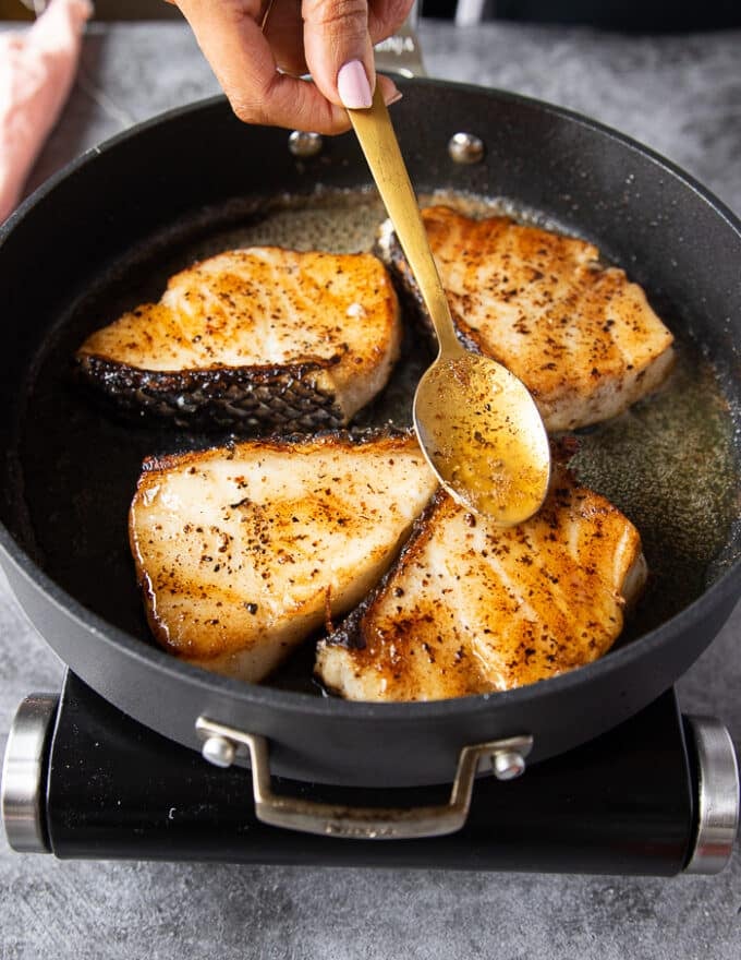 a spoon spooning in the butter from the pan on to the chilean sea bass while cooking