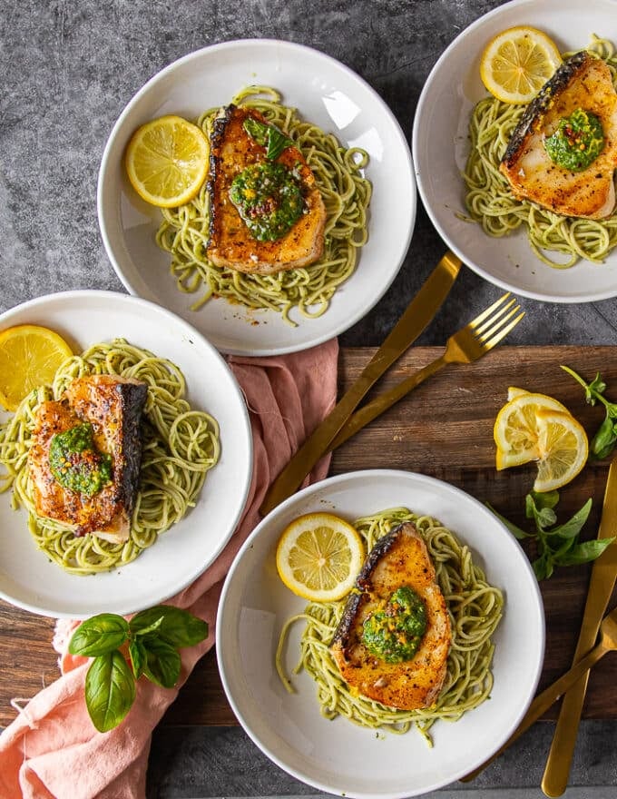 4 plates of served chilean sea bass over pesto pasta on a wooden table