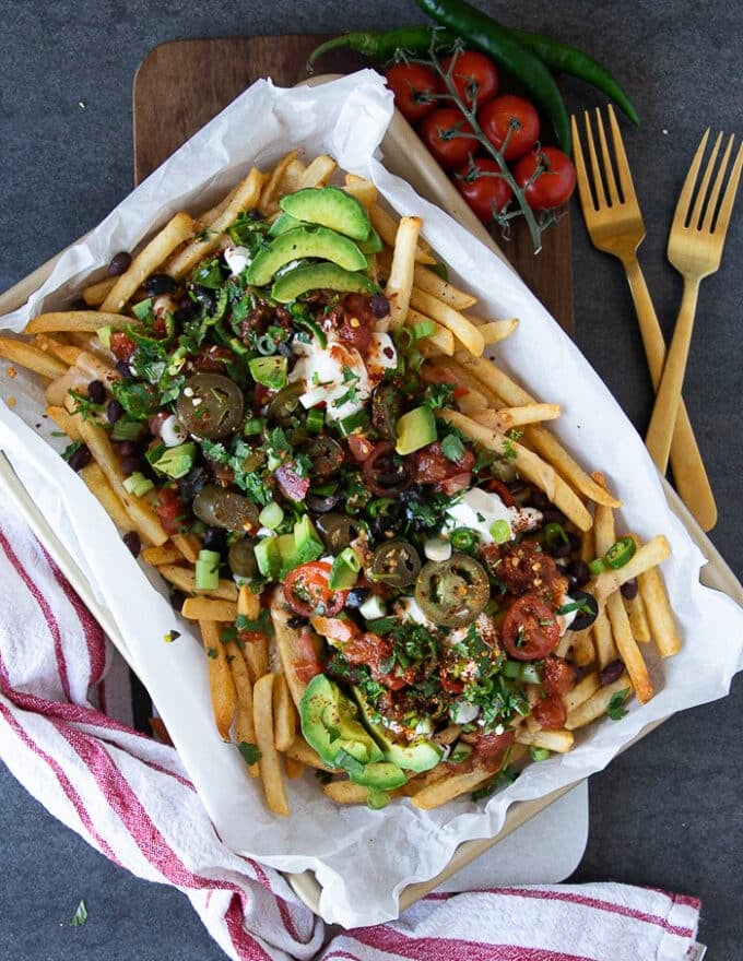 finished plate of nacho fries loaded with toppings and served with two forks
