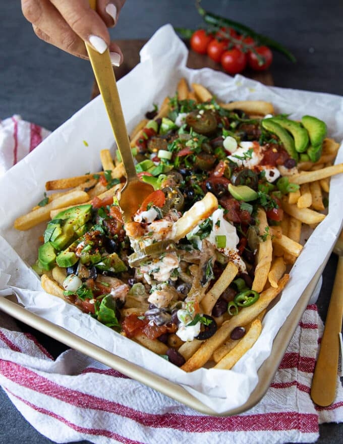 A hand holding a fork grabbing some nacho fries