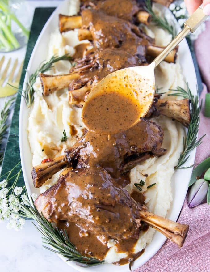 A hand spooning some braising sauce over the braised lamb shanks