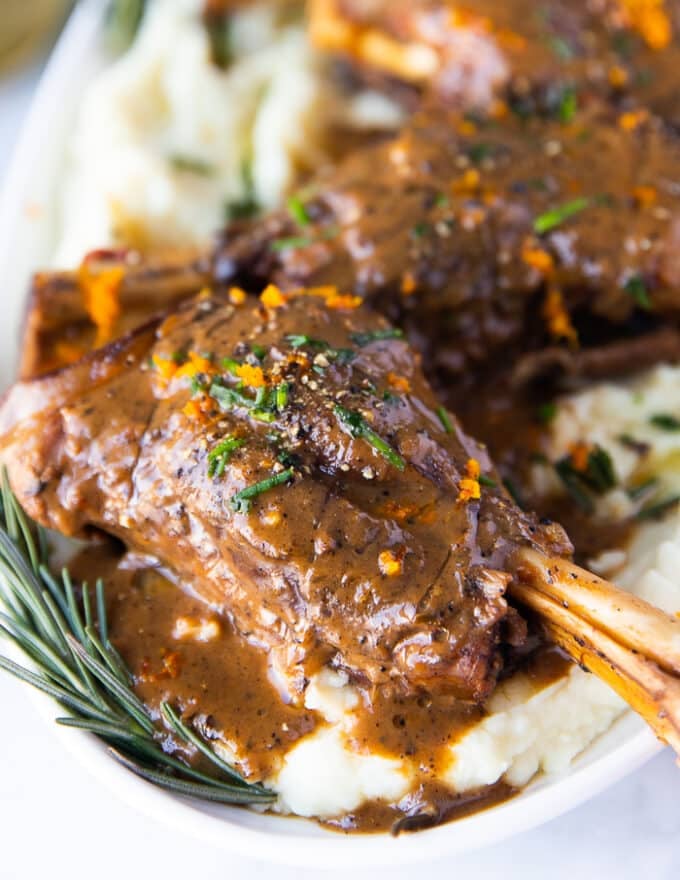 close up of one braised lamb shank served over mashed potatoes and drenched with gravy 