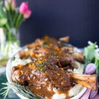 side view of the lamb shanks on a plate surrounded by fresh rosemary